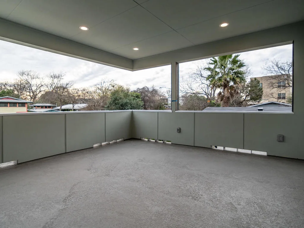 Covered outdoor living space with solid railings and recessed ceiling lights overlooks a neighborhood with trees.
