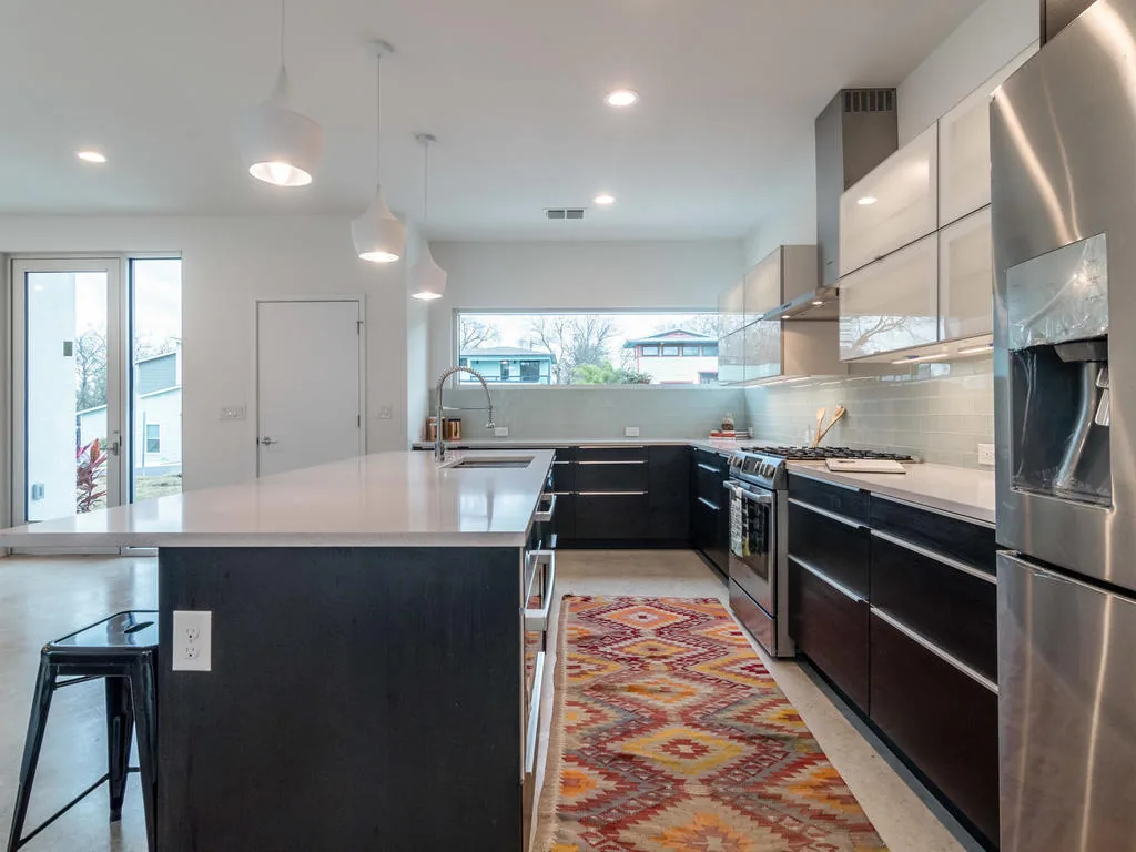 Kitchen featuring a black kitchen island, stainless steel refrigerator, and a marble backsplash under horizontal clerestory windows.