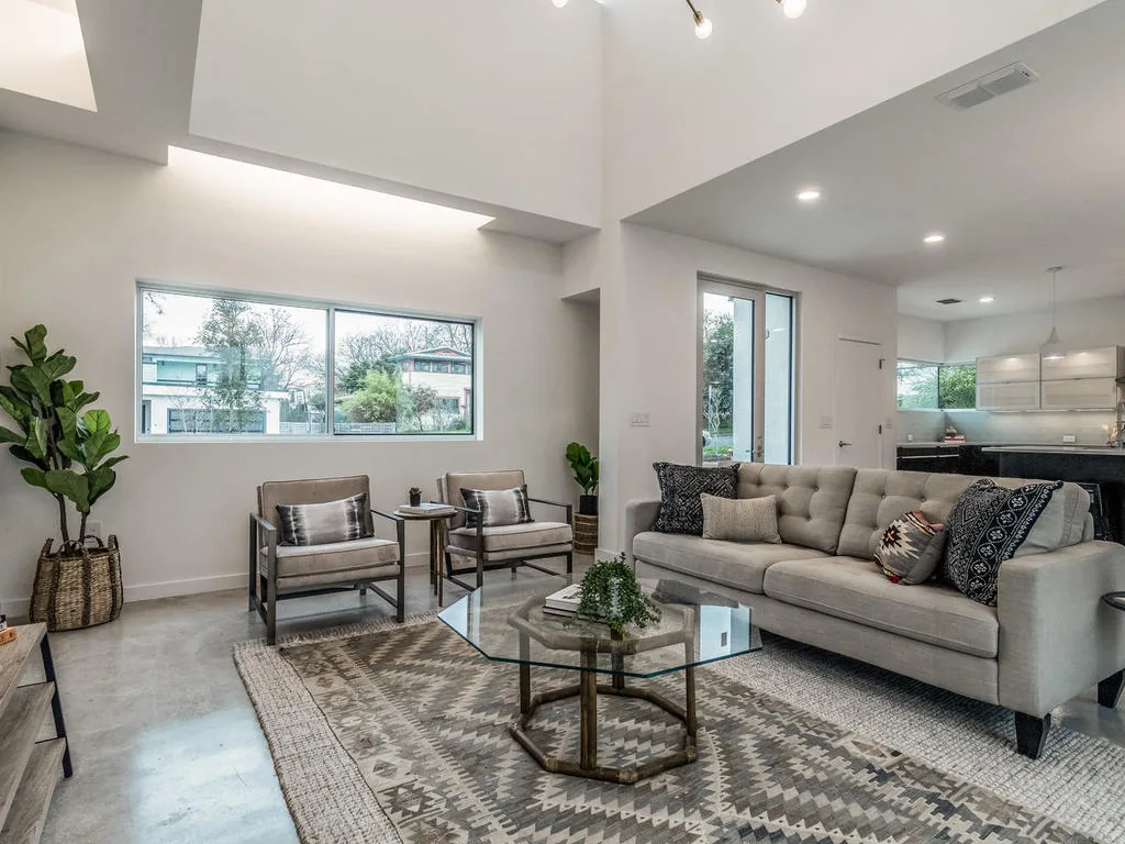 This modern living room features a large gray sofa, two armchairs, and horizontal windows providing natural light.