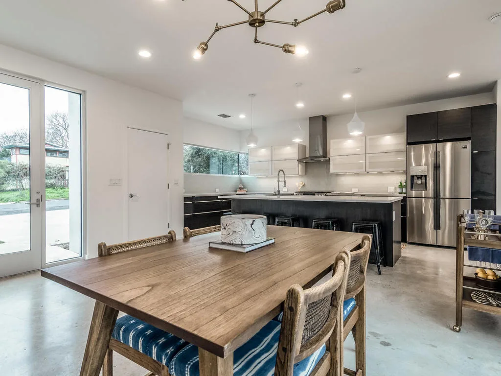 Modern kitchen and dining room with black and white cabinetry, stainless steel refrigerator, and pendant lights above the island.