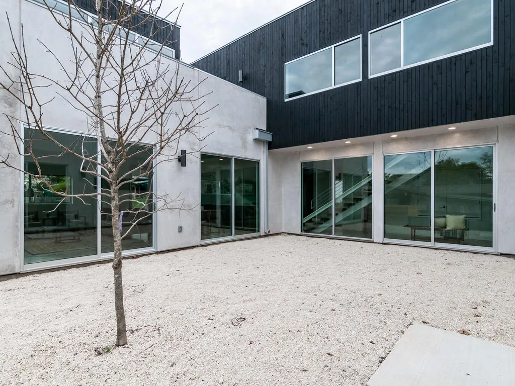 Modern courtyard featuring large glass doors and a gravel ground surface around a central tree.