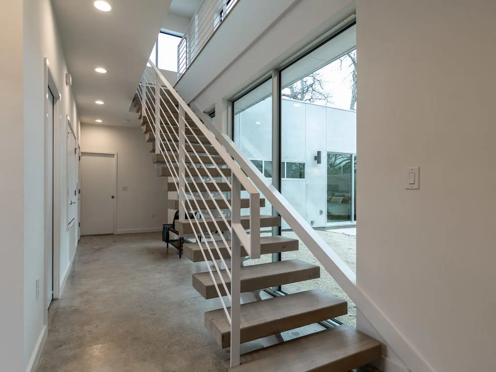 Modern staircase with open risers and large windows overlooking a courtyard.