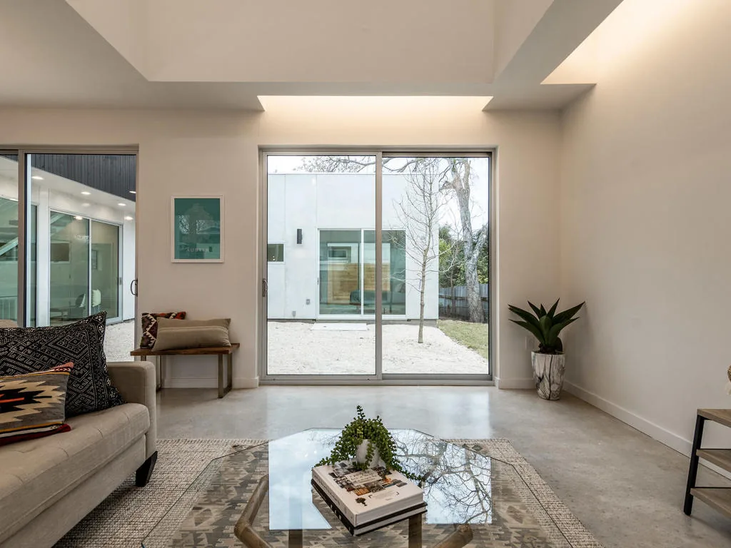 Living room featuring sliding glass doors opening to a courtyard with gravel and a leafless tree in project 410postrd by KRDB.