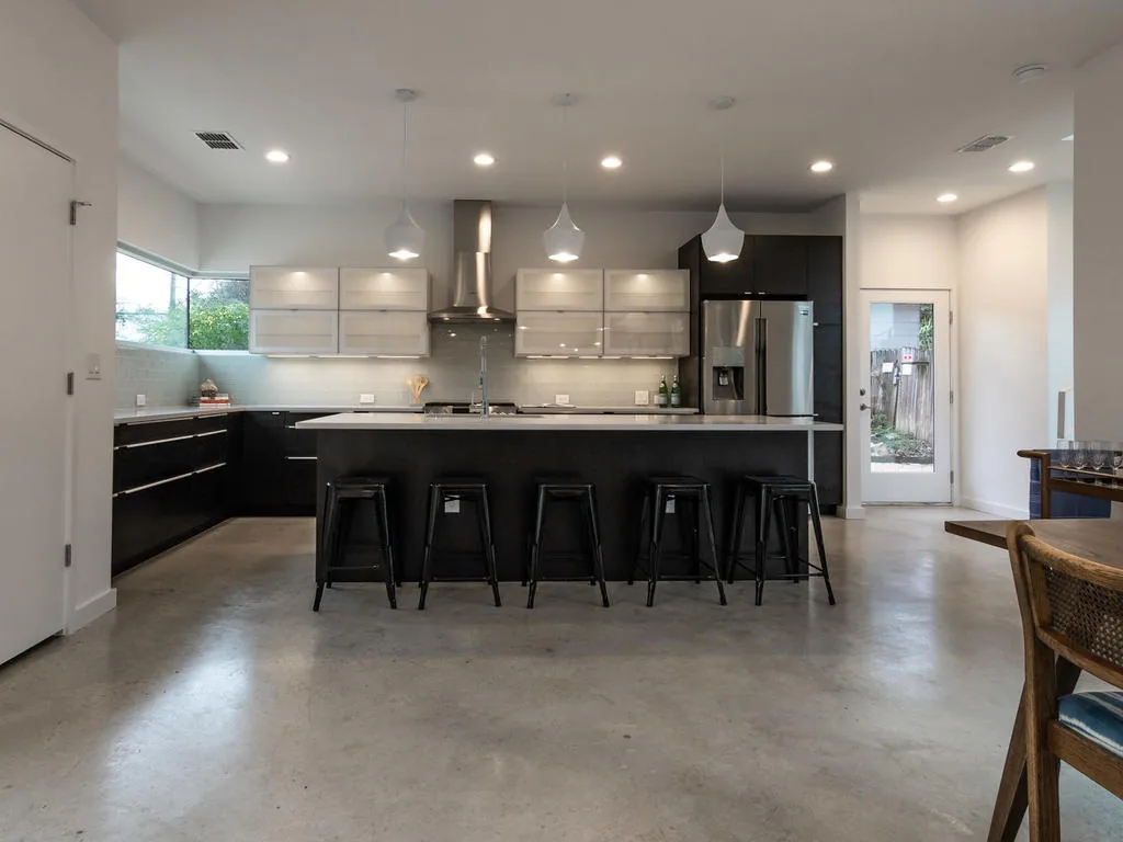 The kitchen features a large island with seating, black lower cabinets, and horizontal clerestory windows providing natural light.
