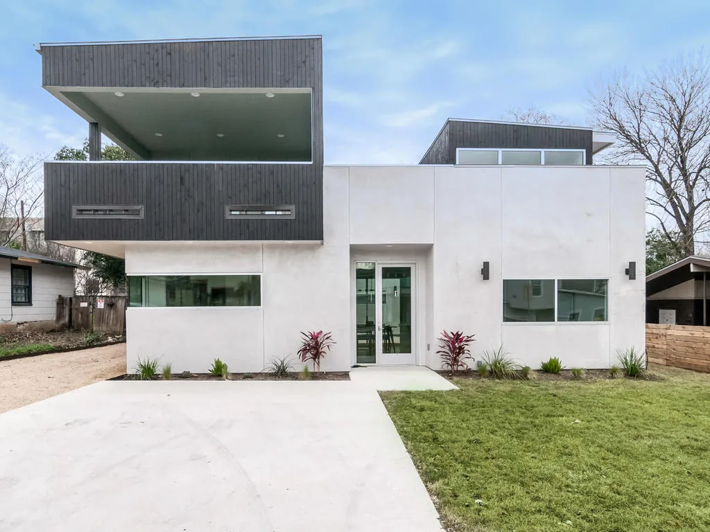 Modern two-story house with white stucco walls and dark wood siding accented by horizontal windows and a recessed entrance.