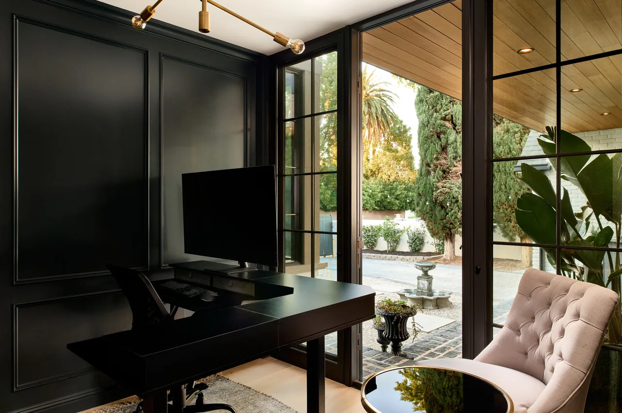 Office space with black furniture and floor-to-ceiling windows opening to an exterior courtyard with plants and fountain.