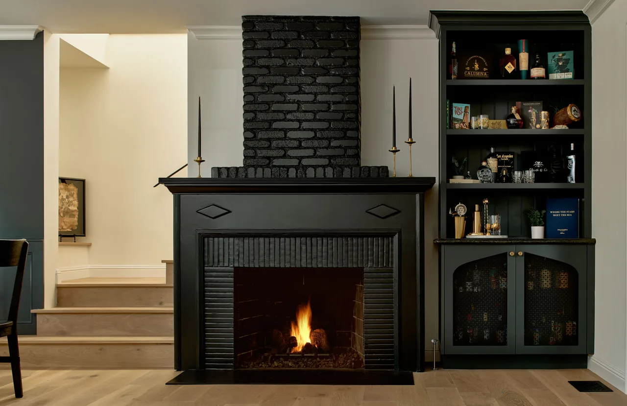 Black brick fireplace flanked by a black built-in cabinet and shelves with decorative items.