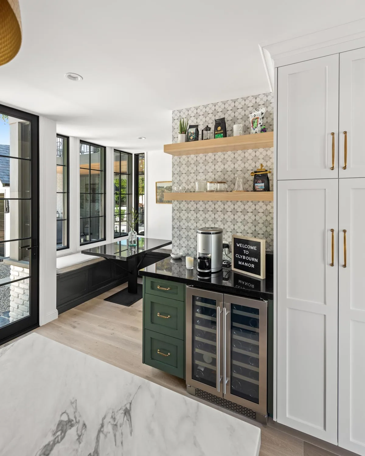 Kitchen area features black-framed windows, patterned tile backsplash, green lower cabinets, and wooden open shelves.