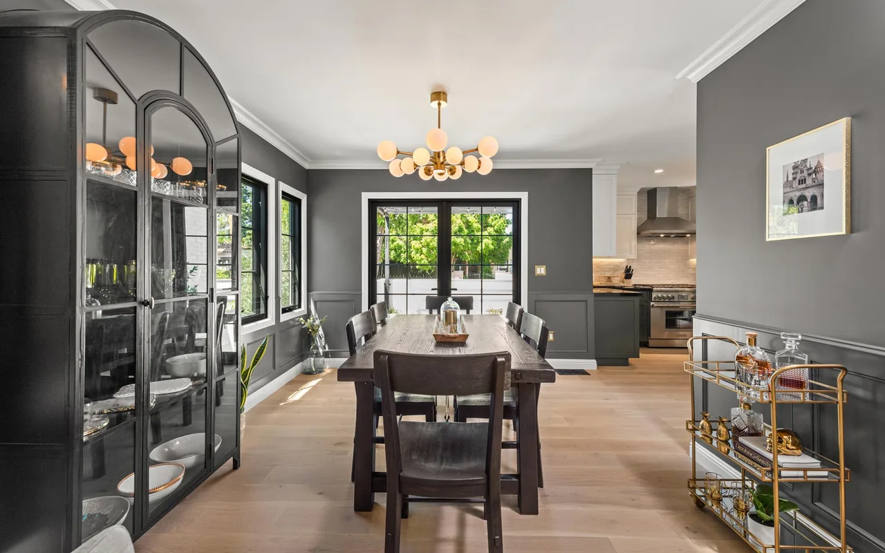 Dining room with dark gray walls, glass cabinet, and modern chandelier adjacent to kitchen area.