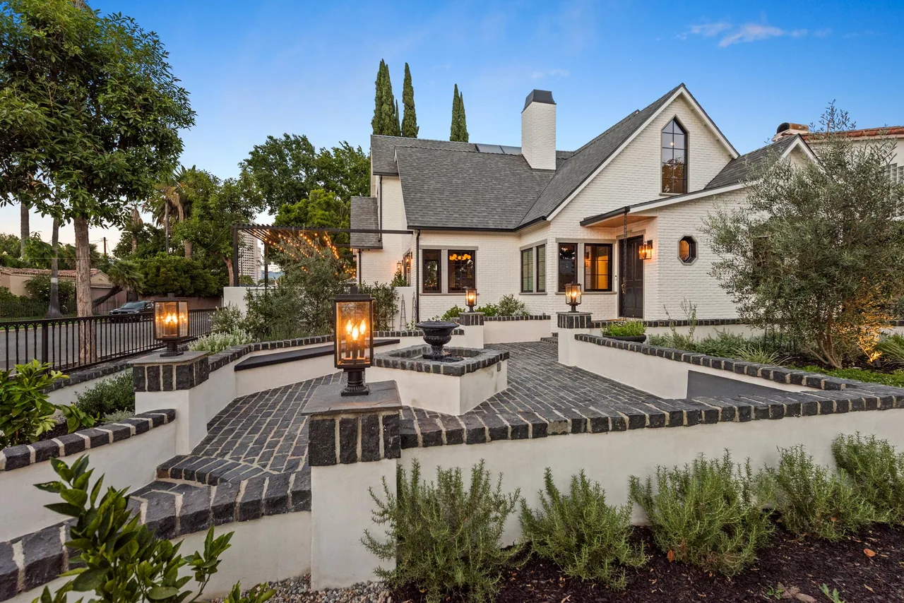 Exterior front view of a white brick home with a courtyard featuring black brick coping and integrated lighting lanterns.