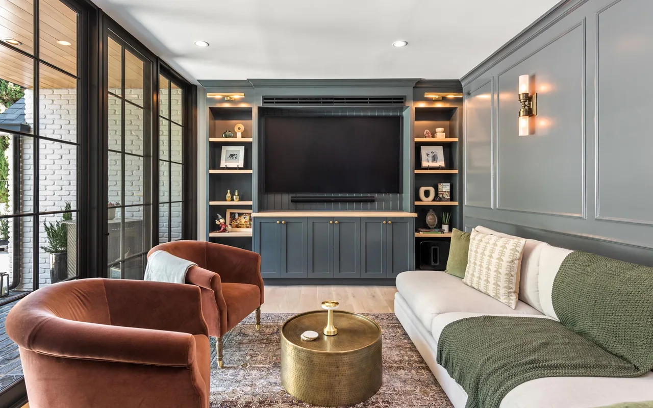 Living room with gray paneled walls, built-in shelving, and large windows shows modern and traditional elements combined.