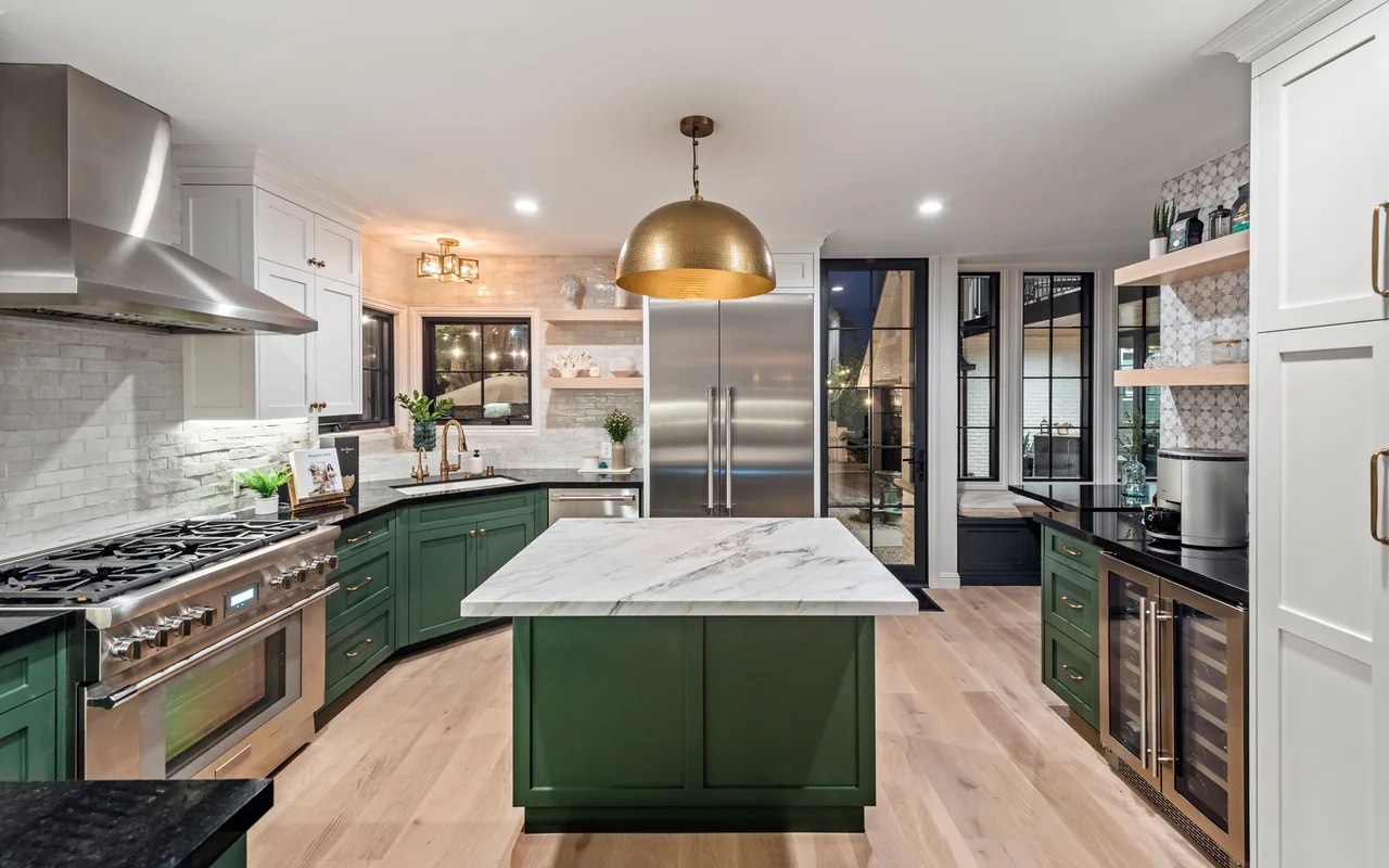 Kitchen with green lower cabinets, marble island, stainless steel appliances, and gold pendant light in the Clybourn Manor project.