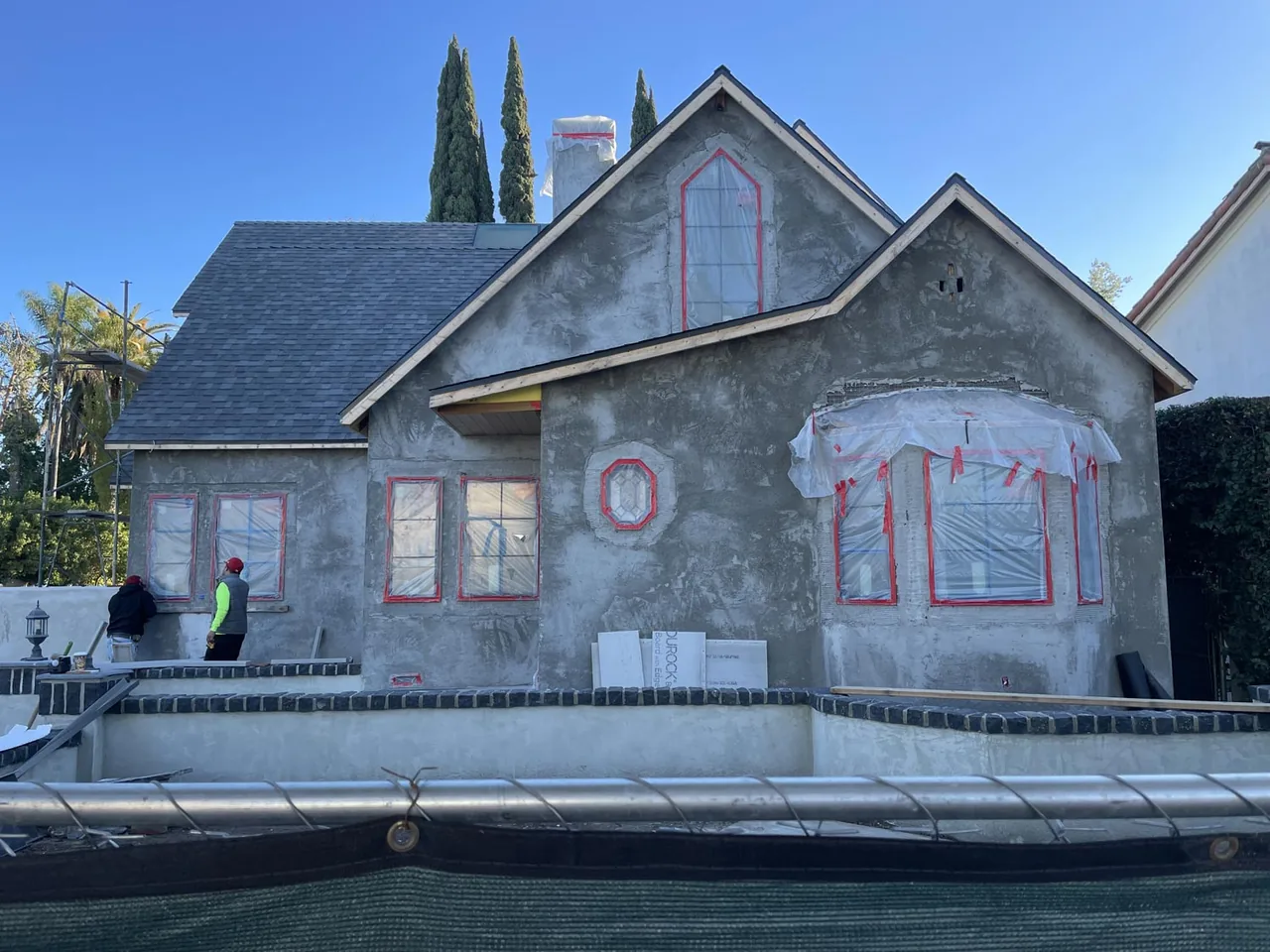 Exterior front view of Clybourn Manor house in early stucco phase with protective coverings on windows and black brick planter walls.
