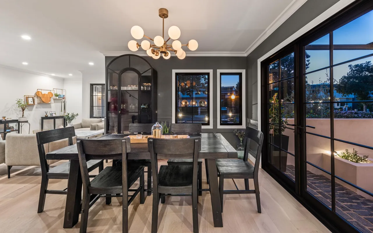 Modern dining room featuring dark wooden furniture, black window frames, and a brass pendant light, adjacent to an outdoor patio.