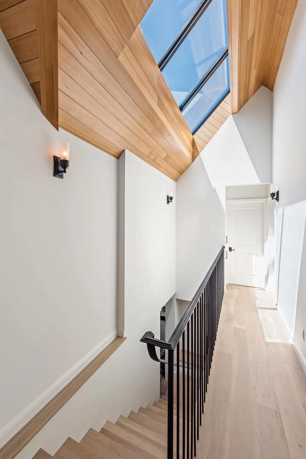 Hallway and staircase with wood-paneled vaulted ceiling and skylight allowing natural light.