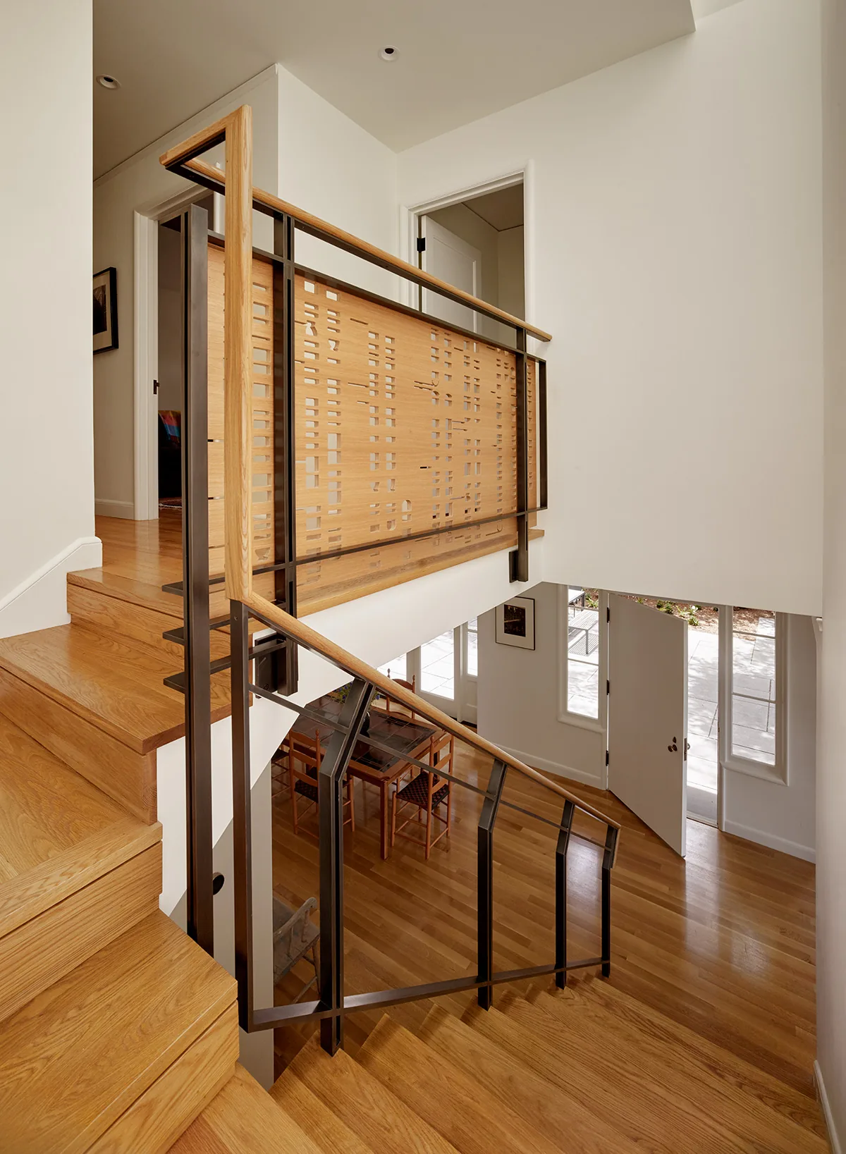 Staircase with wood flooring, custom wood and metal railing, and an entry door at the bottom level in the Claremont Canyon Residence.