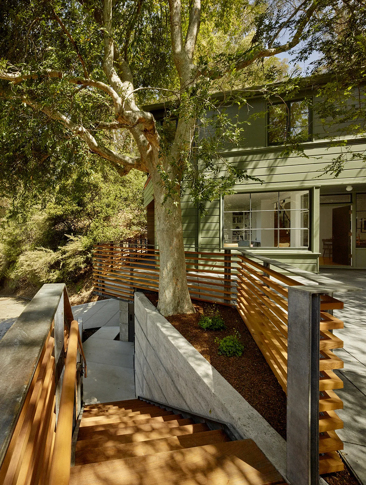 Green siding and wood railings highlight the exterior of the Claremont Canyon Residence with a shaded outdoor stair area.