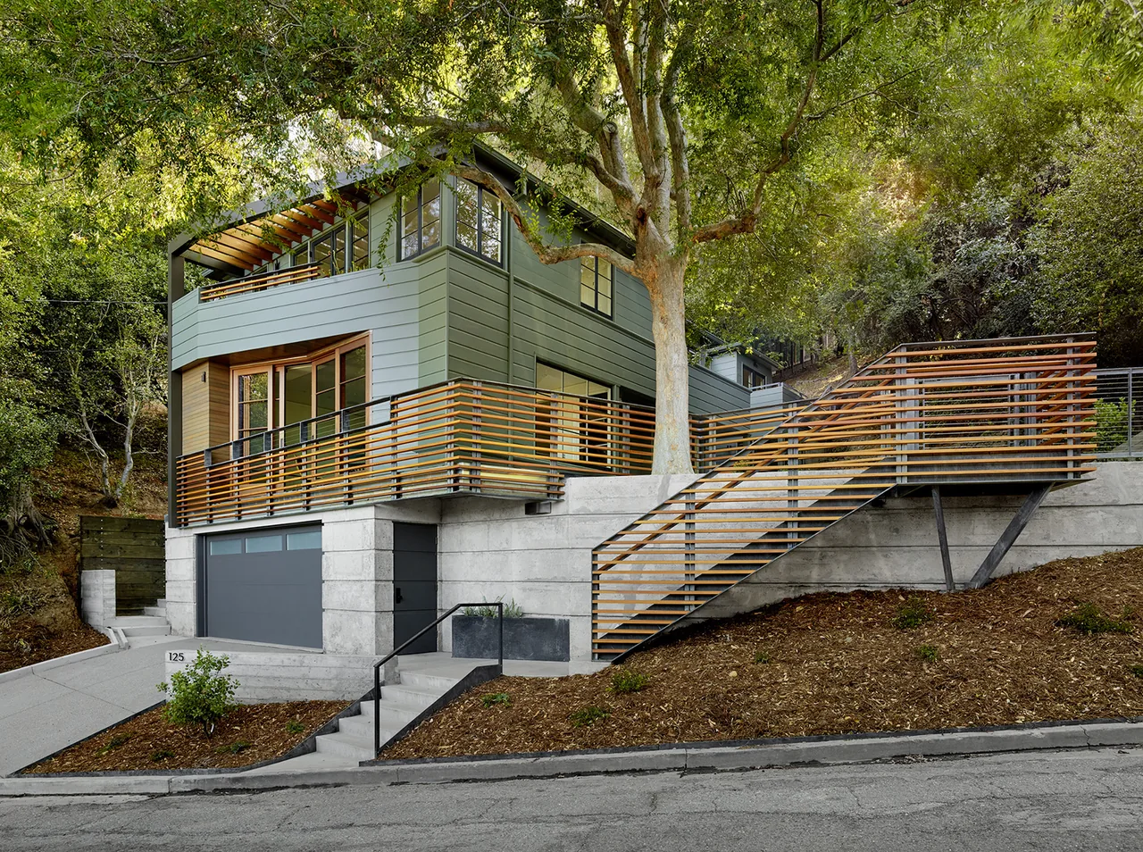 Claremont Canyon Residence features green siding with extensive horizontal wood railing and concrete foundation in hillside setting.