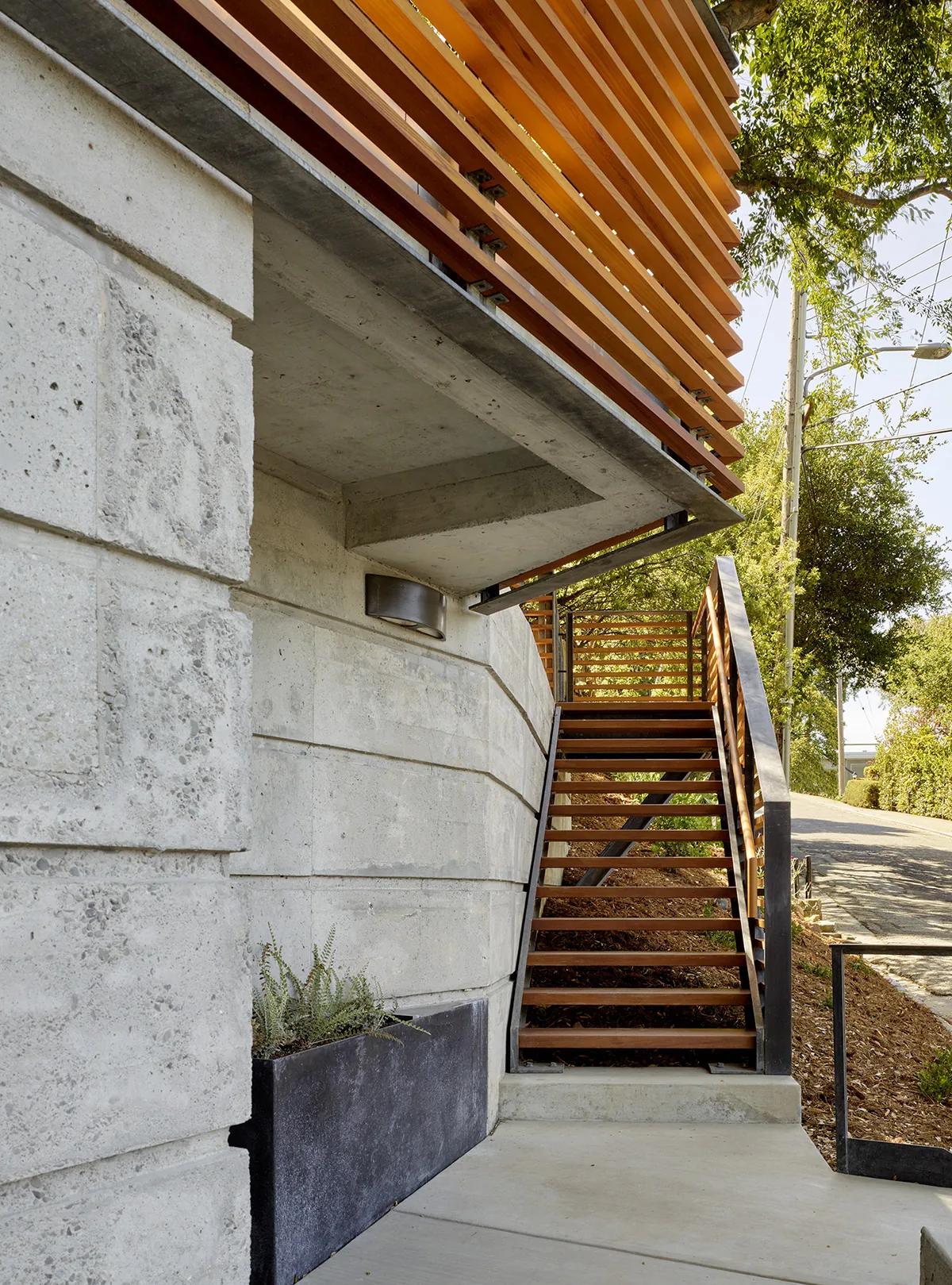 Exterior stairway with wood treads and metal railing ascends alongside a concrete wall at Claremont Canyon Residence.