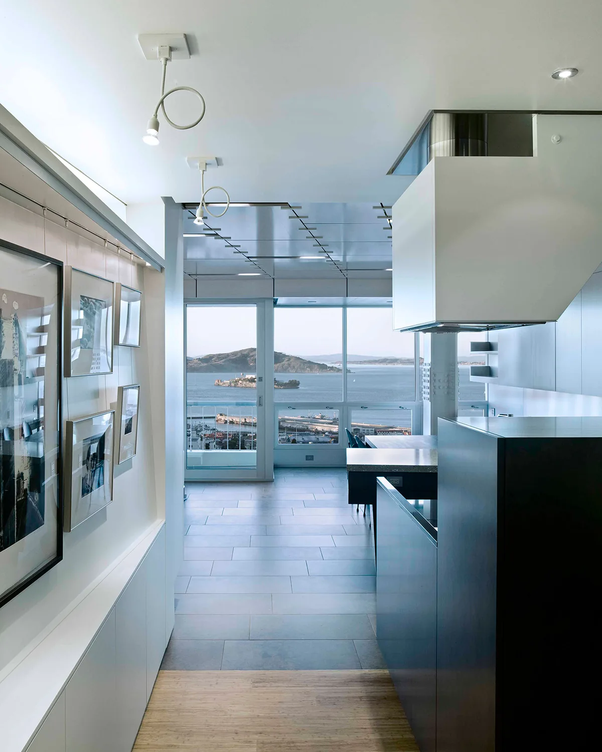 Hallway view looking toward dining area with floor-to-ceiling windows overlooking a waterfront and hilly landscape.