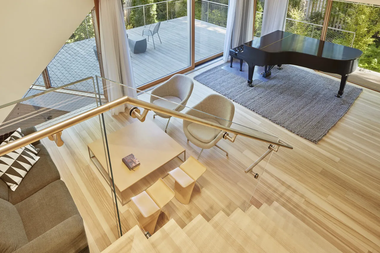 Open living area with a grand piano near large sliding glass doors leading to a wooden deck outside.