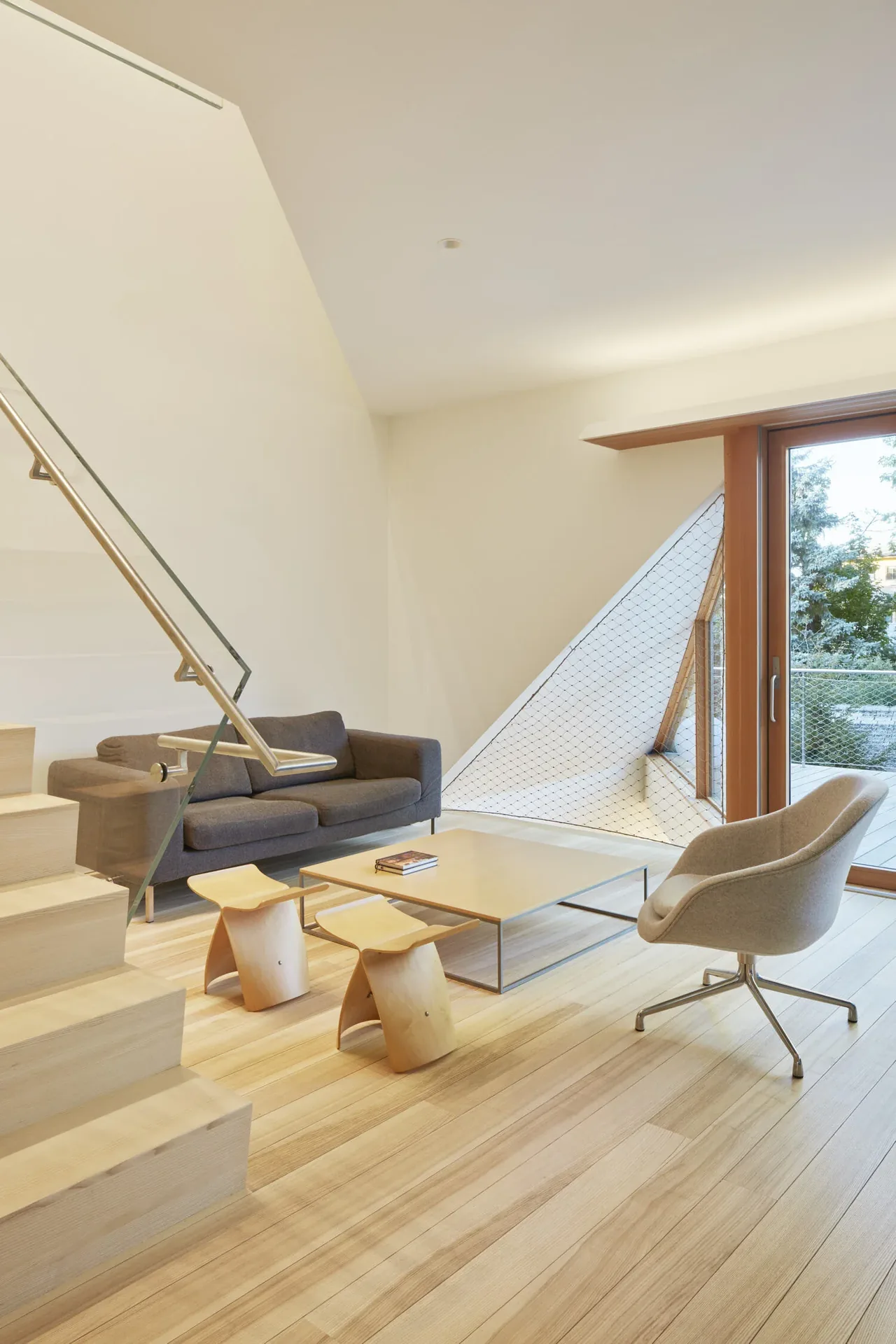 Living room with minimalist wood floor and furniture, featuring a large sliding glass door leading outside.