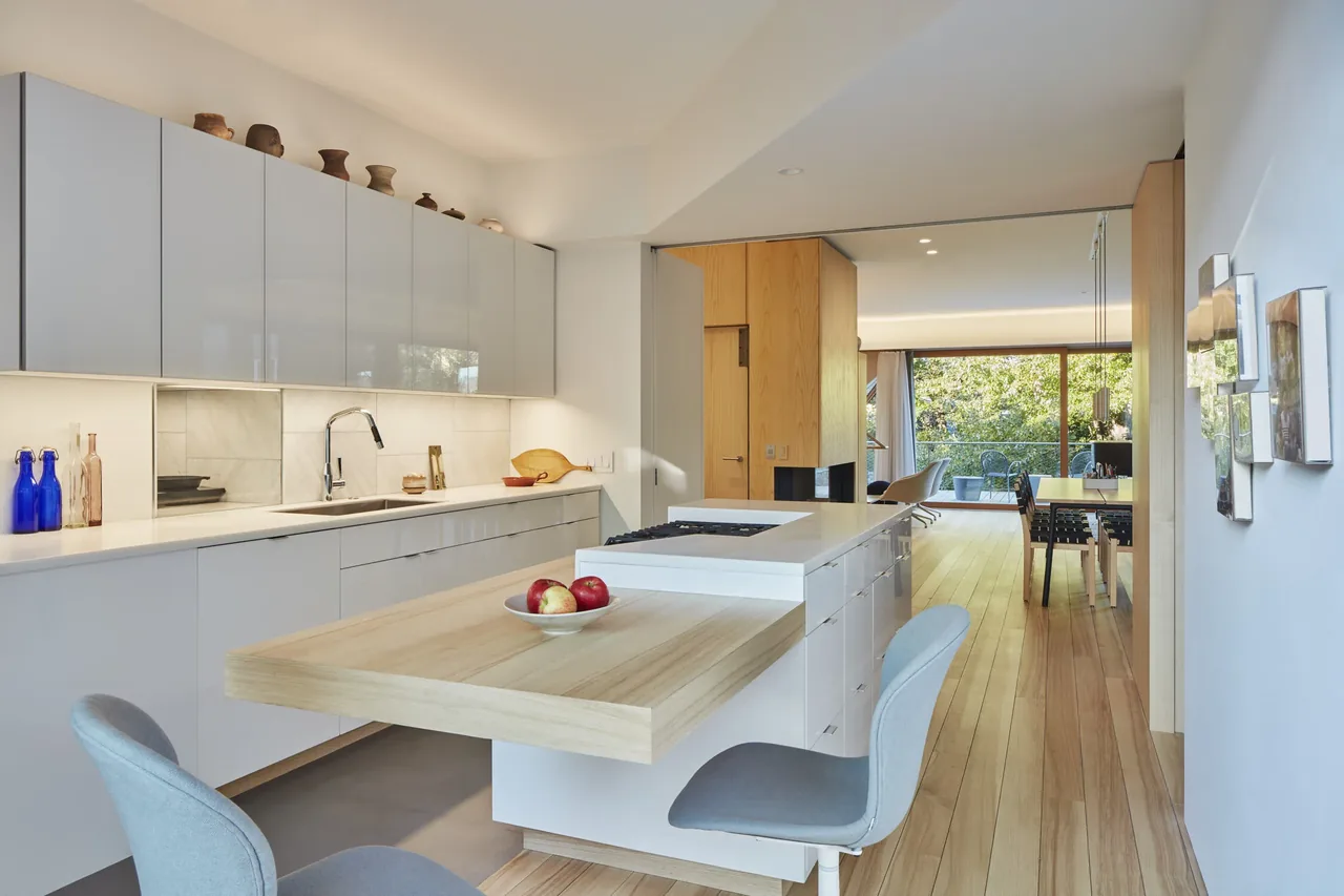 Modern kitchen features white cabinetry, wood island extension, and large windows opening to a dining area with wood flooring.