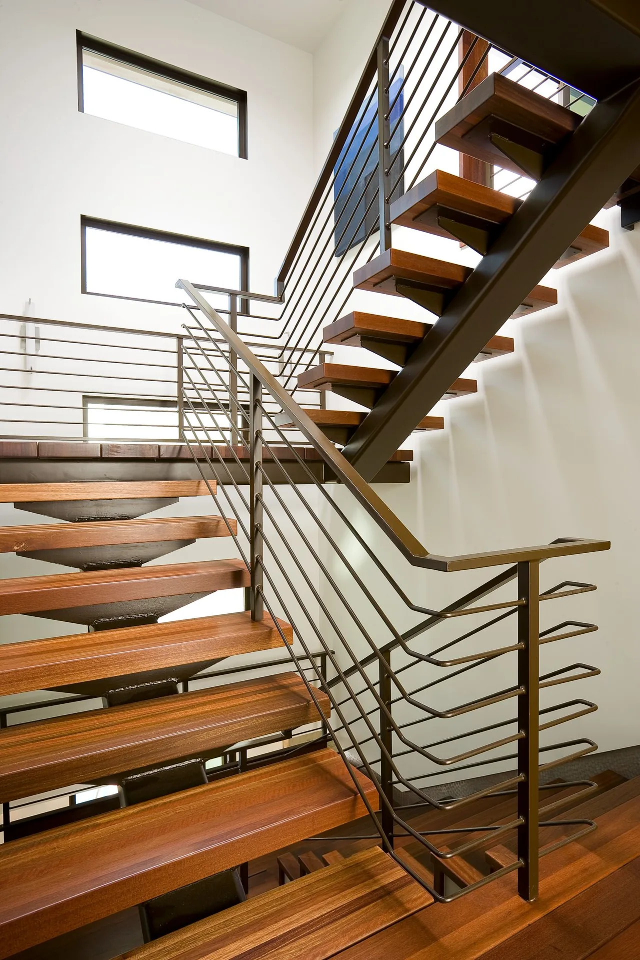 Modern staircase with floating wooden steps and metal railing inside a home with clerestory windows.