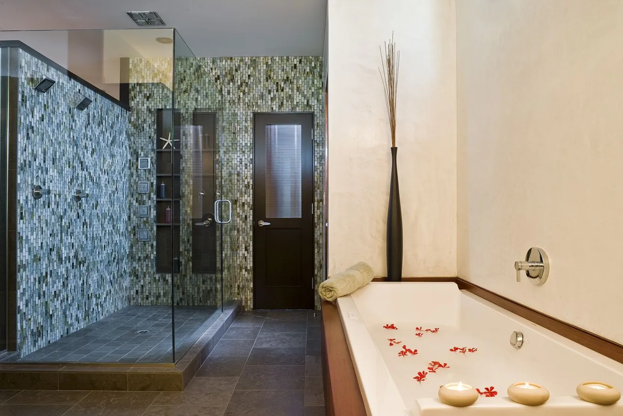 Bathroom featuring a glass shower enclosure with mosaic tile walls and a bathtub accented by candles and flower petals.