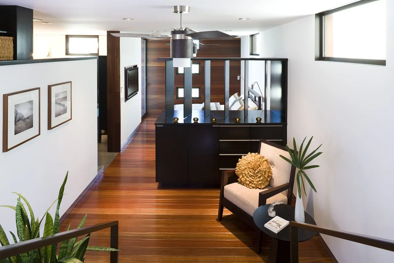 Interior hallway space with wood flooring, armchair seating, and partial view of a bedroom through a glass divider.