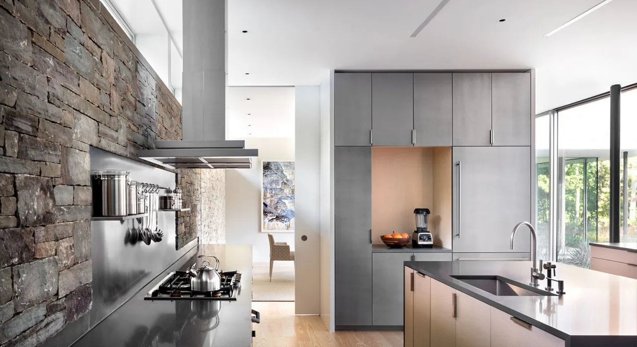Kitchen features a dark stone accent wall, gas range cooktop, and gray flat-panel cabinetry adjacent to a large window.