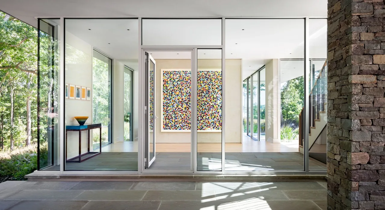 Hill House entrance with full-height glass walls and door opening to an art-filled interior hallway.