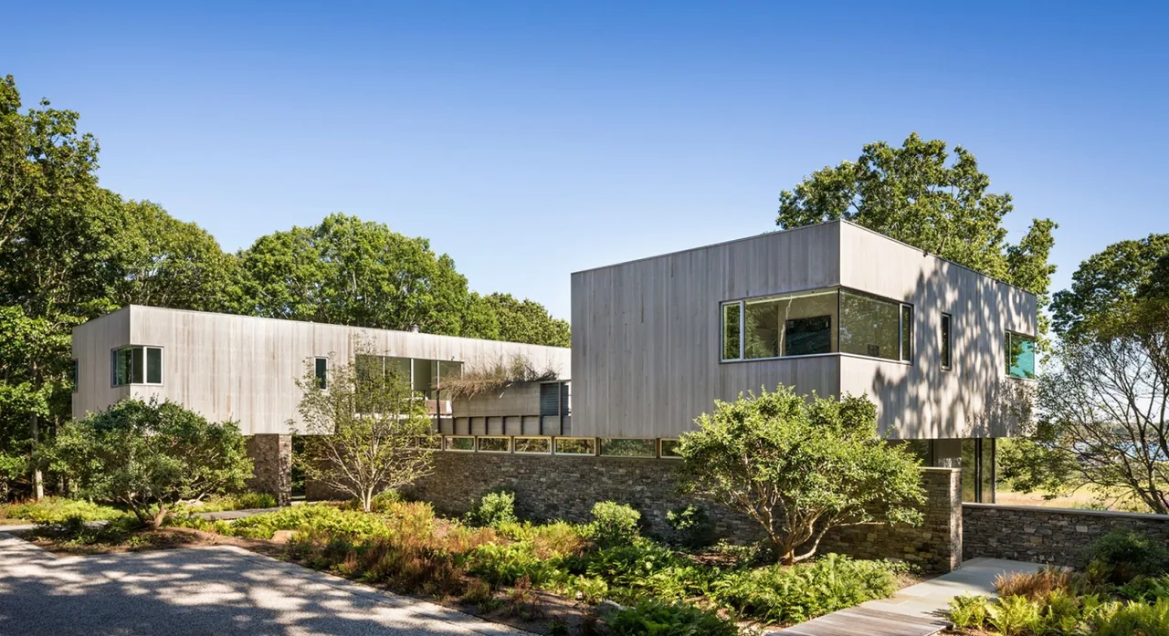 Hill House features two modern rectangular volumes with light wood siding above a stone base, surrounded by natural landscaping.