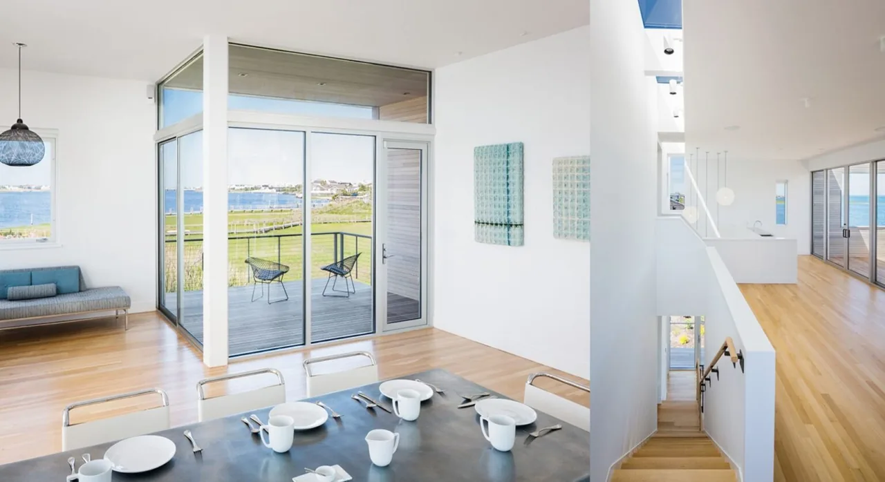 Open interior space with dining area, sliding glass doors, wood flooring, and views of a balcony and waterfront.