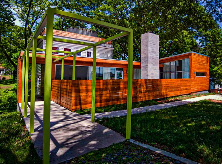 The Beals Residence features a wooden siding exterior with a green metal pergola structure and a stone chimney.