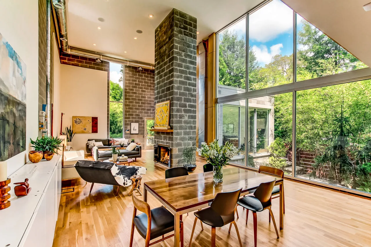 490 Glen Iris features a living and dining space with a large floor-to-ceiling window and exposed brick fireplace by Lightroom.