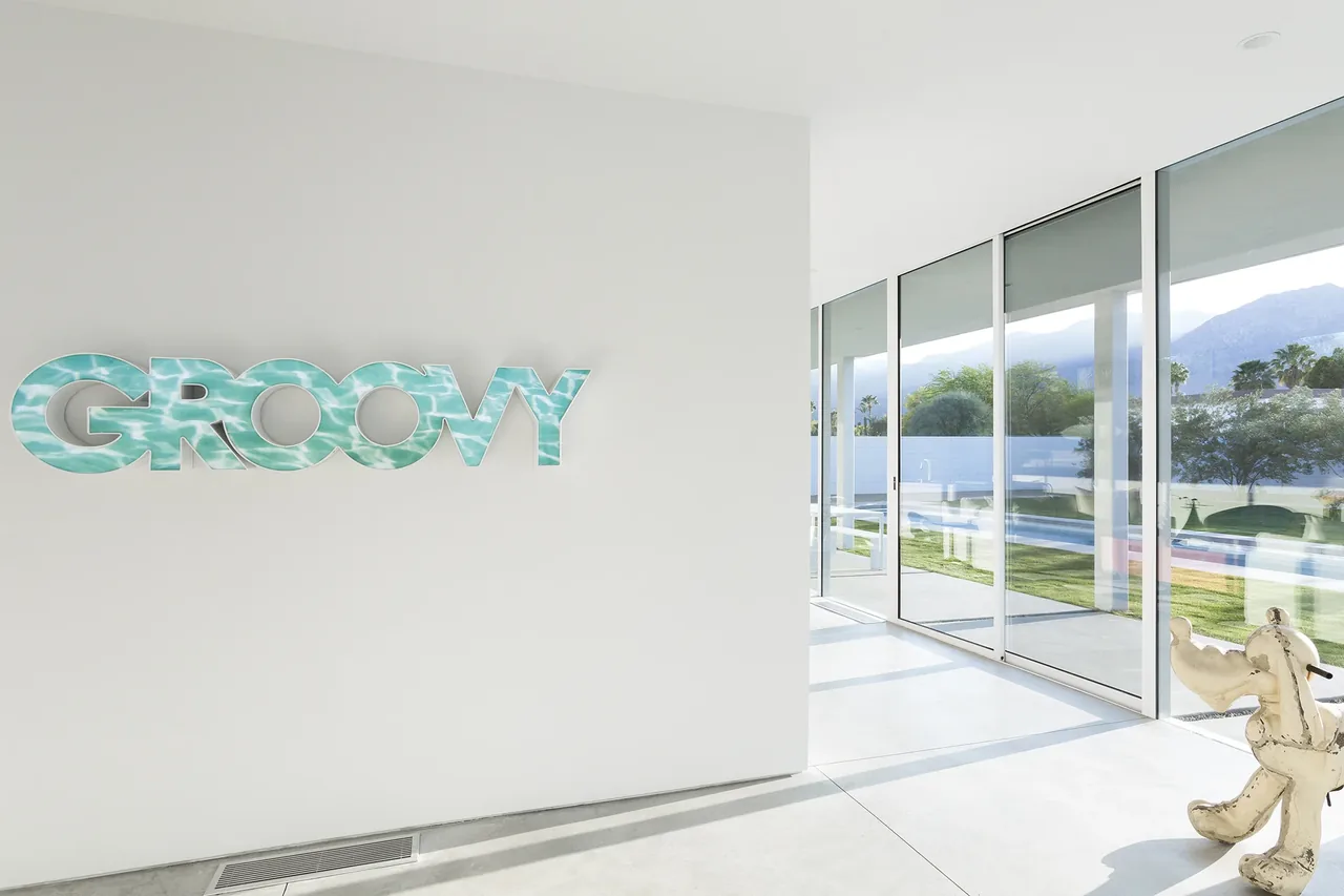 A modern interior featuring a large 'GROOVY' wall sign and floor-to-ceiling glazing overlooking a pool and mountain backdrop.