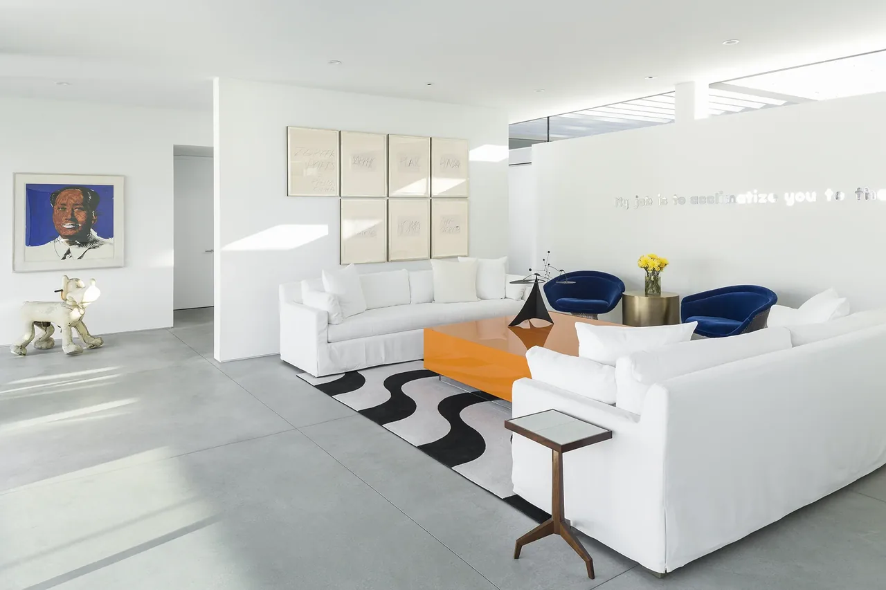 Living room with white sofas, an orange coffee table, and two blue chairs in a bright, contemporary space.