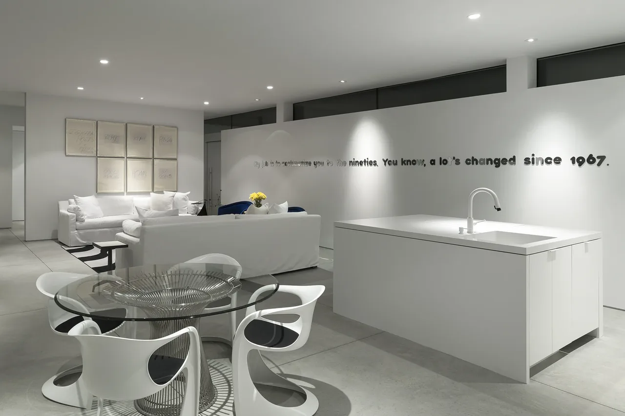Open plan kitchen and living space features a white kitchen island, glass dining table, and white seating with modern decor.