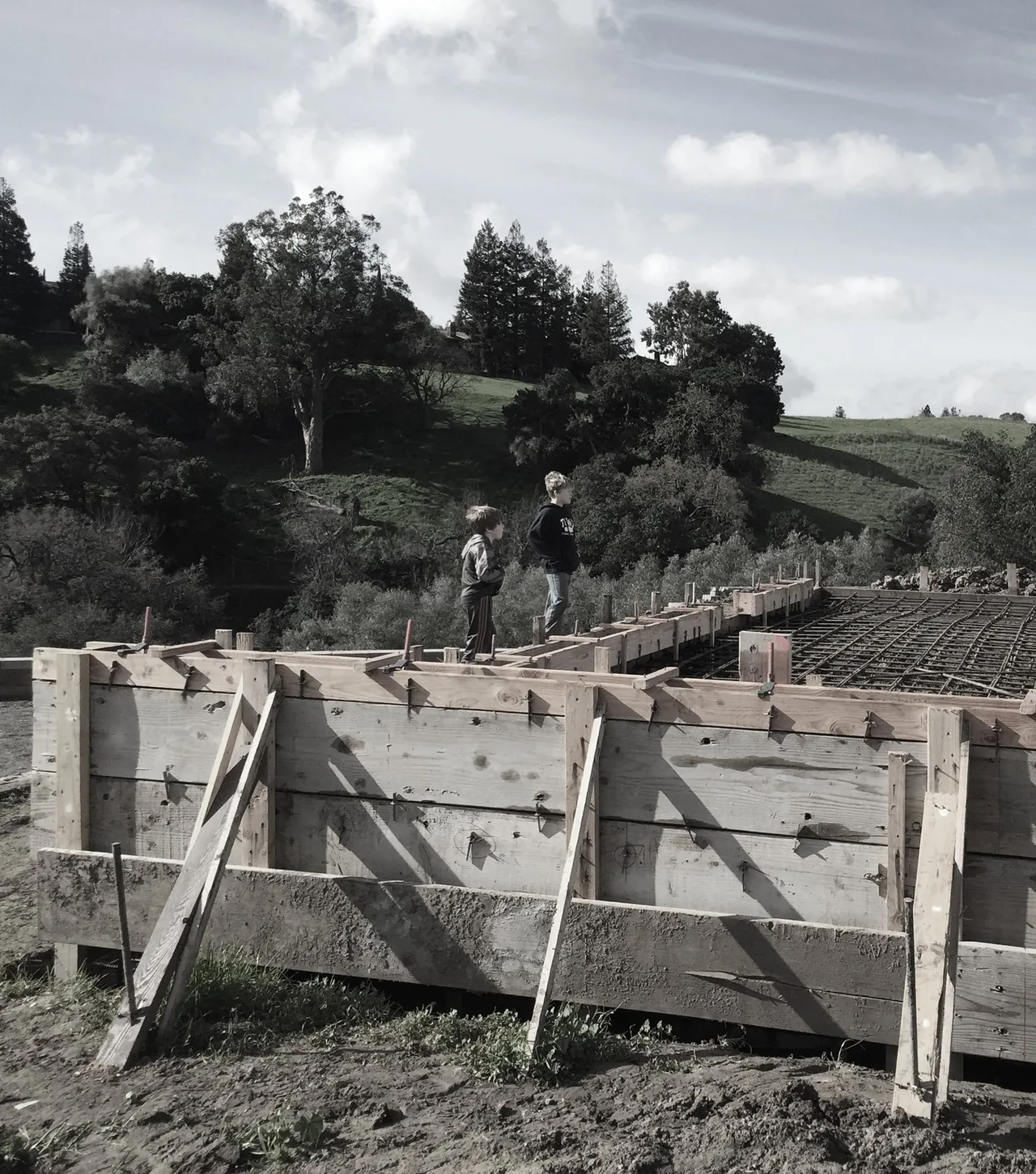 Wooden formwork and rebar prepared for concrete foundation in a hilly outdoor setting.