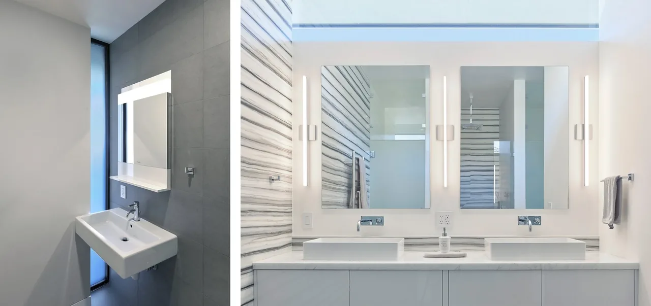 Bathroom featuring vessel sinks, wall-mounted faucets, and vertical light bars beside mirrors in a sleek tile and marble setting.