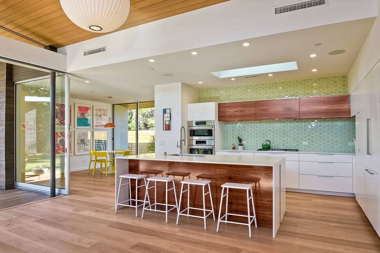 Kitchen with wood and white cabinets, green hex tile backsplash, and white island seating four white stools beneath a round pendant light.