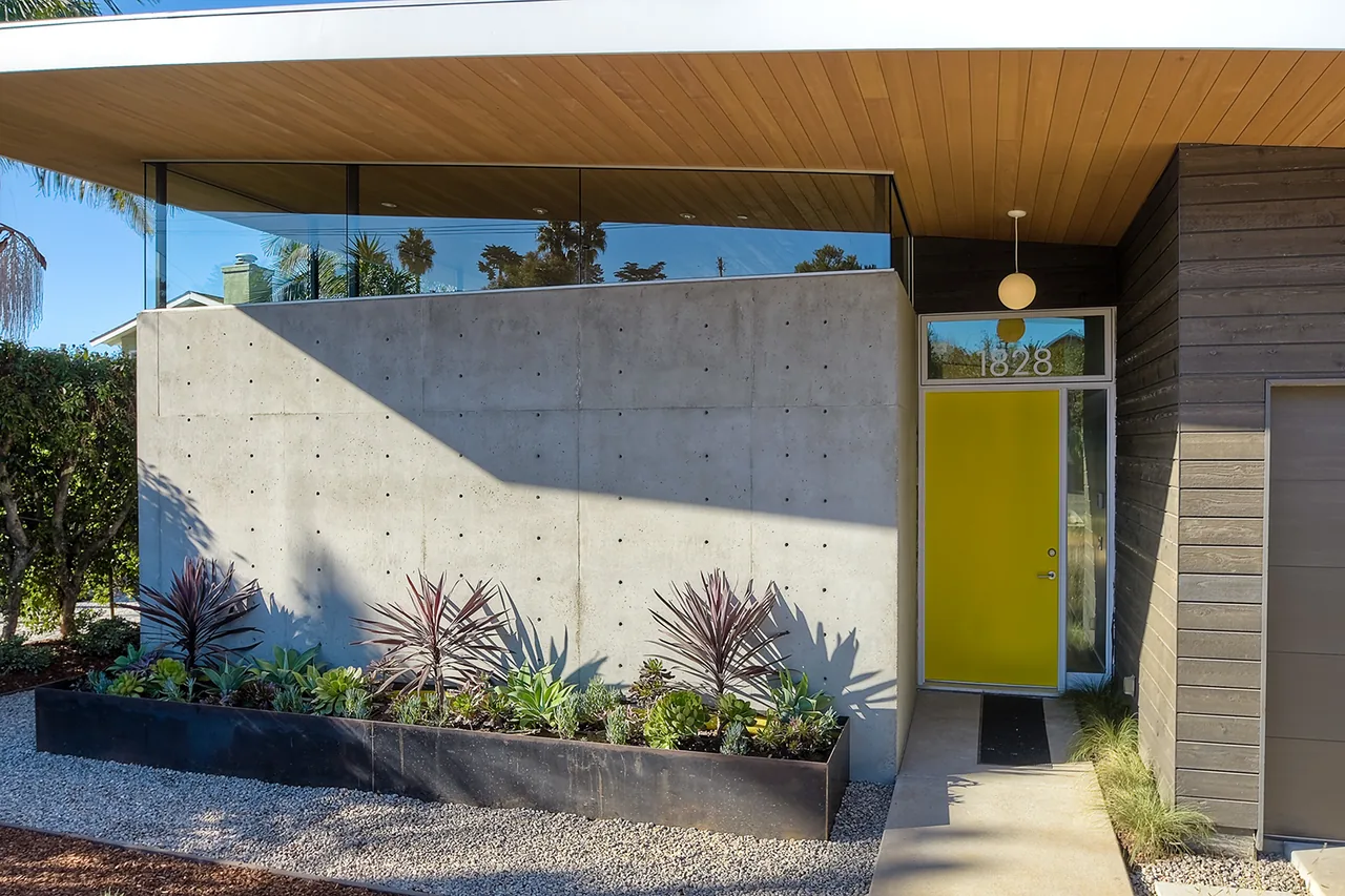 Modern house exterior featuring a yellow entry door, concrete planter, and wood ceiling detail above the entrance.
