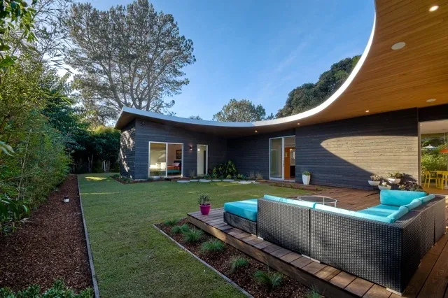 Modern house exterior with wood siding and a distinctive curved wood ceiling overhang over a patio deck area.