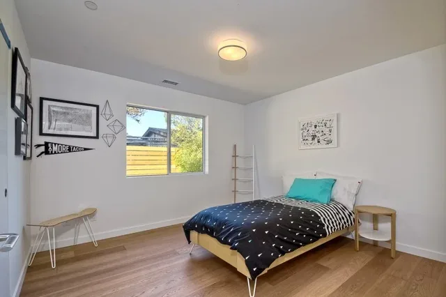 Aa House bedroom with wood flooring, white walls, and simple modern furnishings.