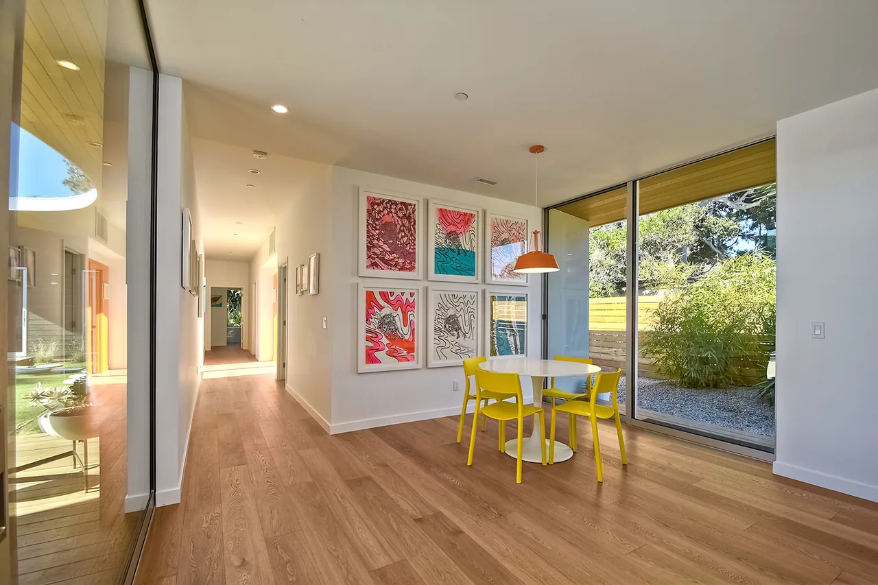 The dining area features a round table with yellow chairs and large sliding glass doors looking out to the garden in Aa House by Lloyd Russell AIA.