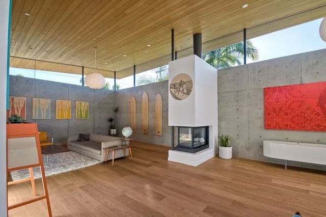 Living room in Aa House features wood panel ceiling, concrete walls, and a modern central fireplace with glass enclosure.