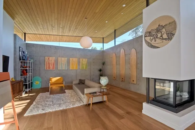 Aa House living room features a wood ceiling overhang, concrete wall, corner windows, and a modern fireplace.