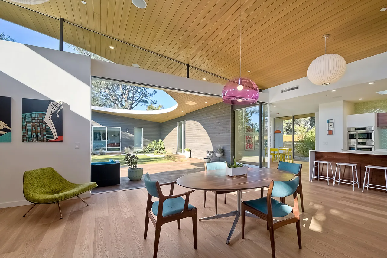 Dining area with wood ceiling and floor seamlessly connects to an outdoor courtyard through large sliding glass doors.