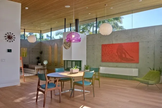 The Aa House dining area features a round wooden table under wood ceiling overhang and concrete walls with clerestory windows for natural light.